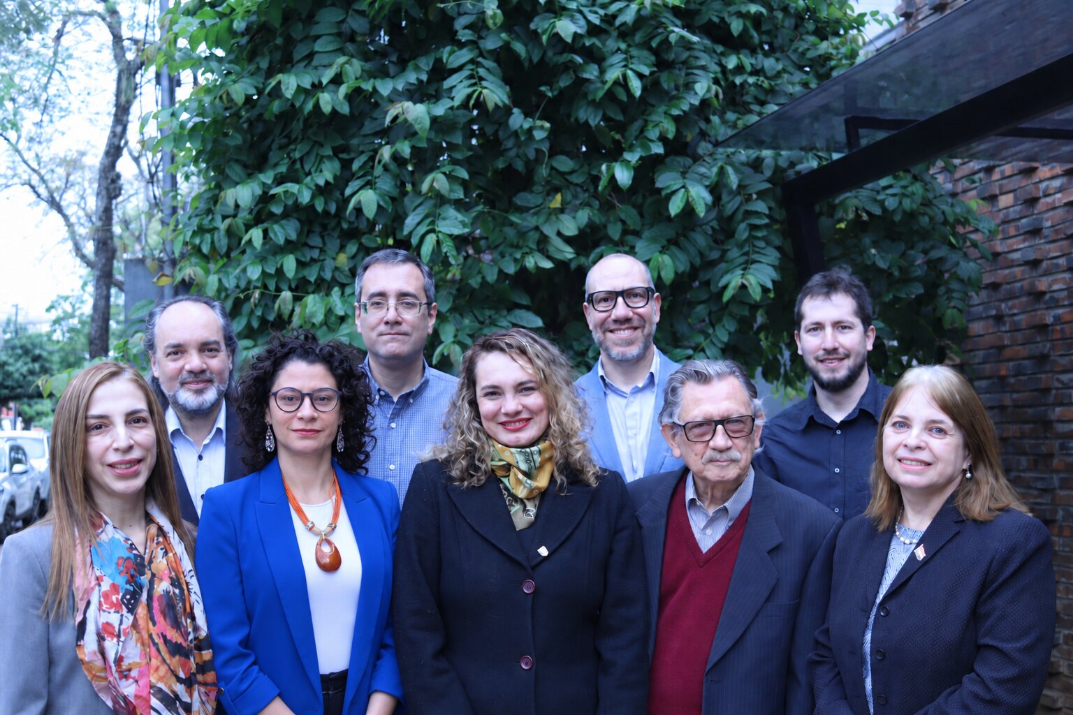 Fotomontaje de los nueve integrantes de INDEX al aire libre, frente a una enredadera junto a la sede