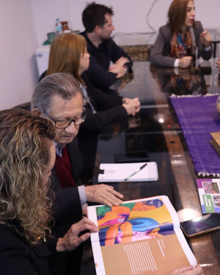 Integrantes de INDEX revisan una revista sobre la mesa de vidrio de la sala de reuniones