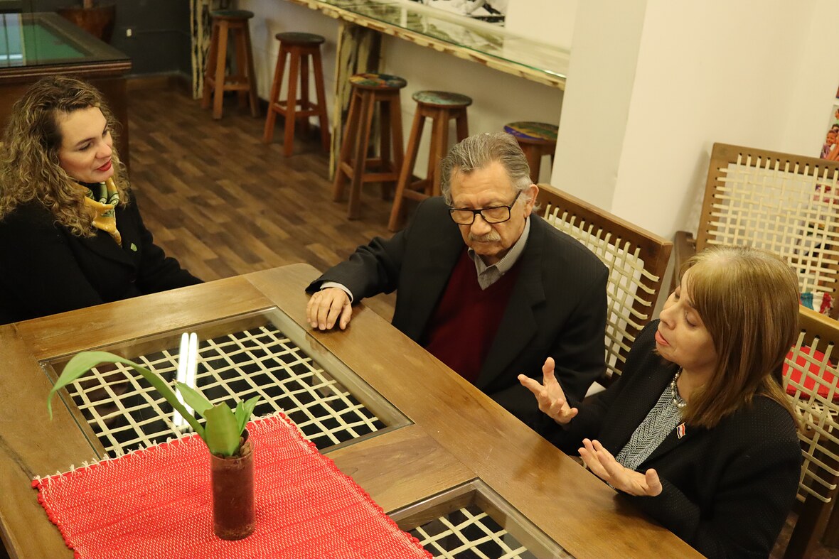 Tres integrantes de INDEX conversan en torno a una mesa de madera en el pasillo de la sede